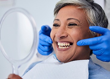 Woman smiling at reflection in handheld mirror