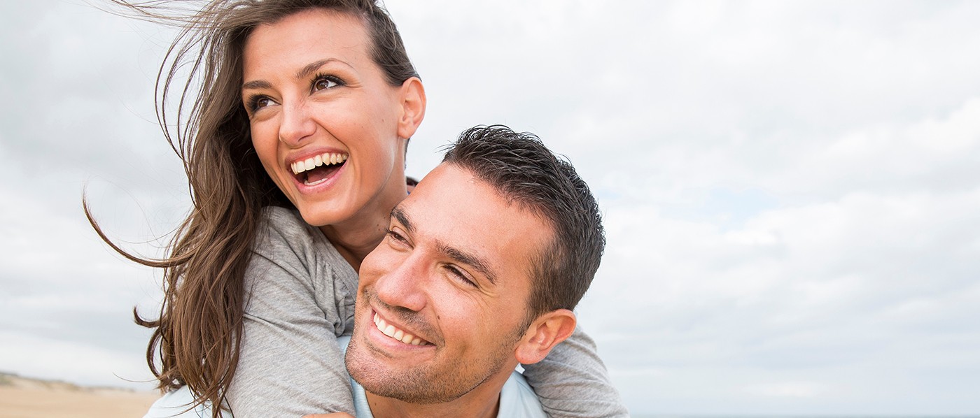 Young couple smiling on beach after using dental insurance in Downers Grove