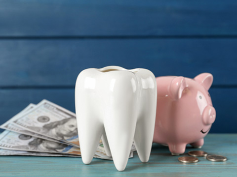 A large ceramic tooth next to a piggy bank, dollar bills, and coins