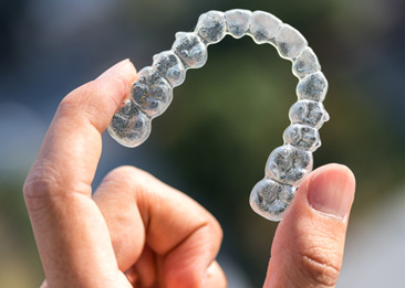A hand holding an Invisalign tray between its fingers