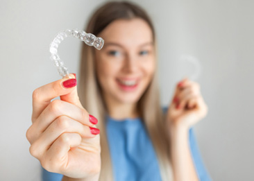 A woman with a non-blurred Invisalign tray in one hand and a blurred one in the other