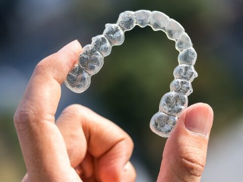 Hand holding an Invisalign aligner outdoors