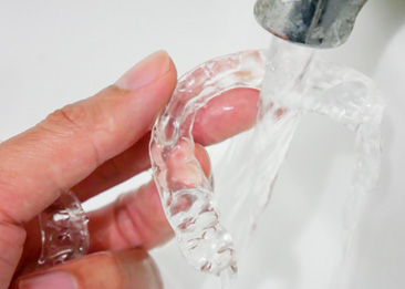A person cleaning their Invisalign aligners with water